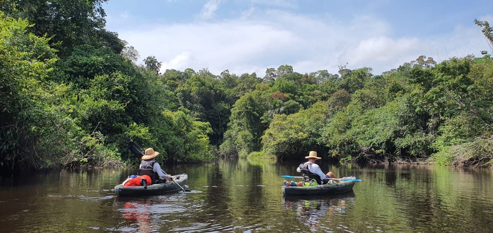 Un kayak, une rivière, et la jungle amazonienne qui referme doucement ses bras. Deux kayakistes en chapeau de paille et gilet de sauvetage pagaient côte à côte sur une rivière calme bordée d'une dense forêt tropicale