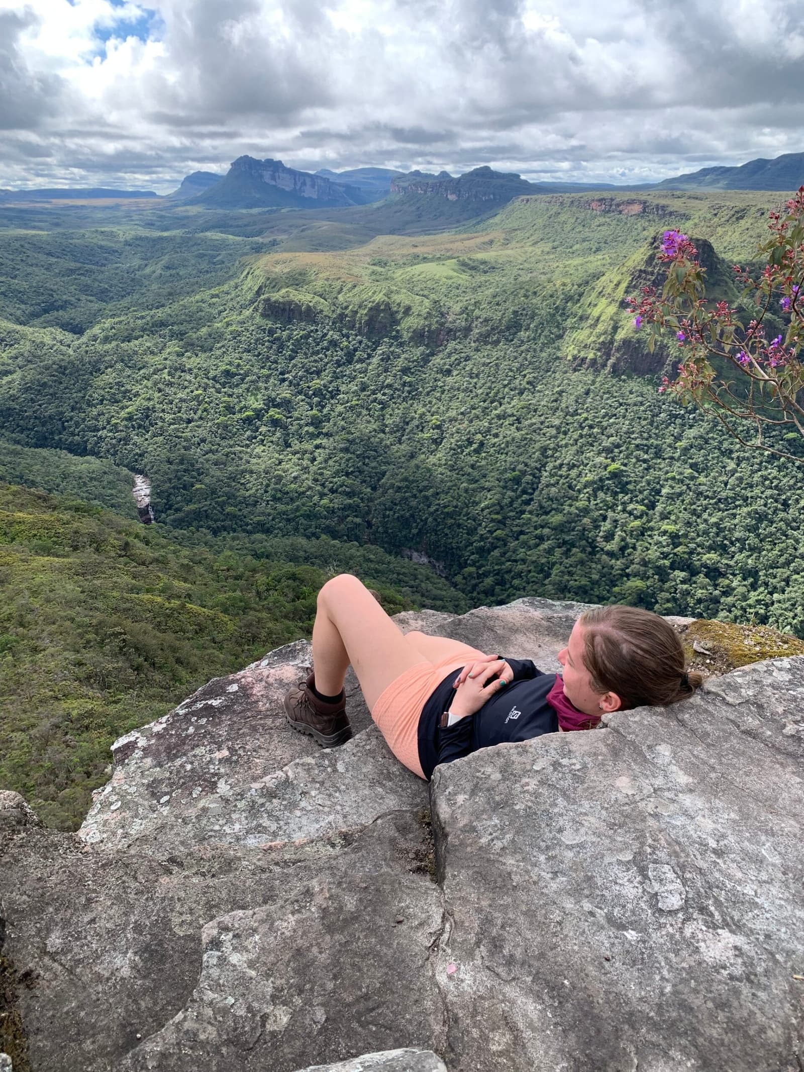 Aussicht verdient, Fels beansprucht. Eine Wanderin liegt flach auf einem Felsvorsprung beim Chapada-Diamantina-Trek und blickt auf einen weiten grünen Canyon mit Tafelbergen und einem fernen Wasserfall
