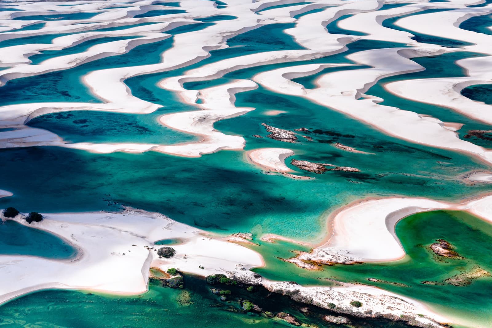Visto de cima, os Lençóis Maranhenses parecem um mapa desenhado por alguém com muita imaginação. Vista aérea do trek pelos Lençóis Maranhenses, mostrando vastas dunas de areia branca entrecortadas por lagoas de água doce turquesa e verde-esmeralda em curvas sinuosas