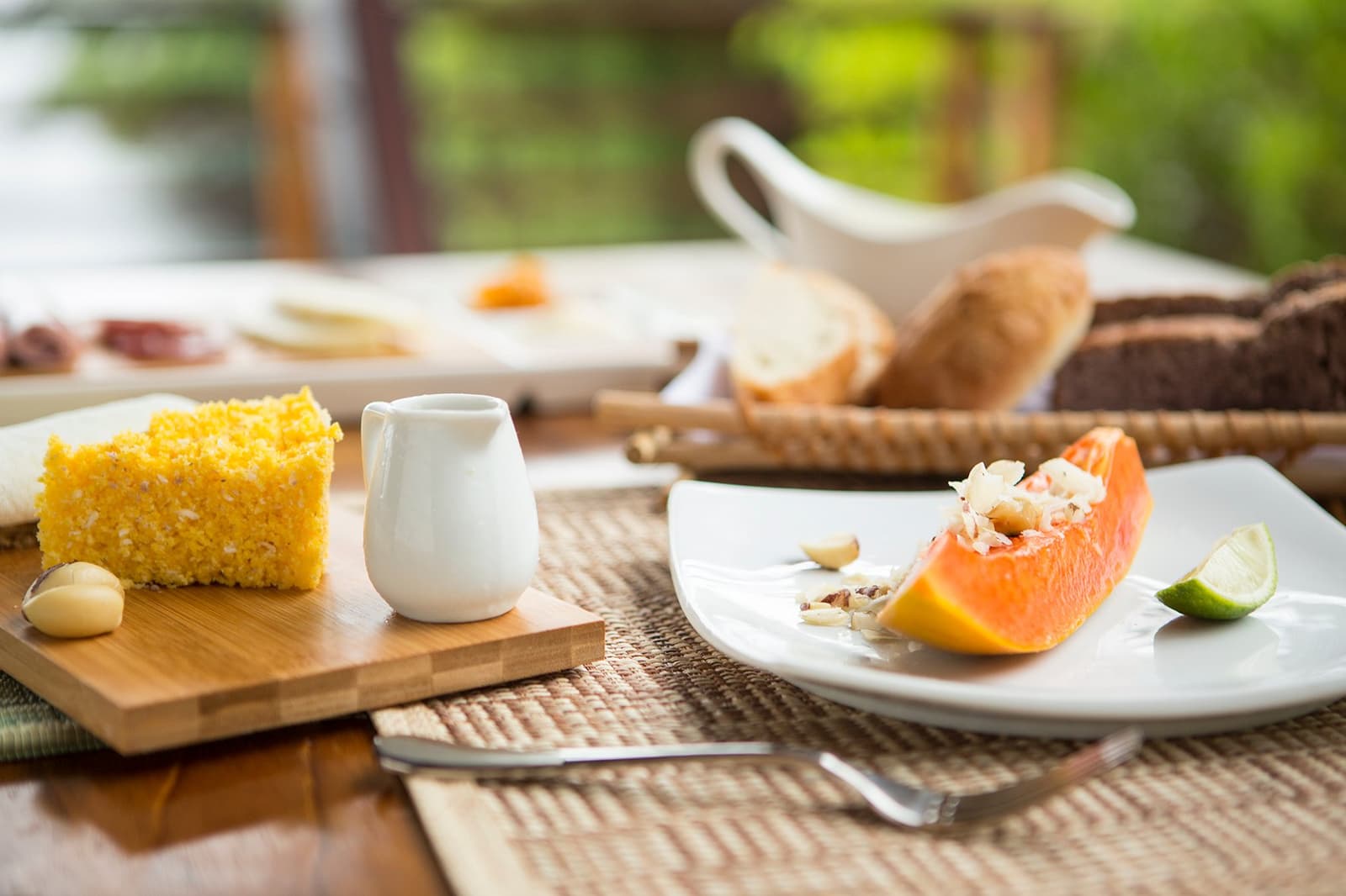 Papaye mûre, gâteau local et vue sur la forêt, le petit-déjeuner qui convainc de rester un jour de plus. Un quartier de papaye garni de noix et de citron vert accompagné d'une tranche de pain de maïs doré sur une planche en bambou, servi au petit-déjeuner au Mirante do Gavião, avec une corbeille de pains artisanaux en arrière-plan