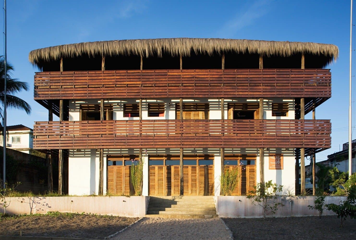 Geniet van het comfort, want morgen begint het bos. Driedraags tropisch gebouw met horizontale houten lattenbalkonnen en een breed cirkelvormig rieten dak, als gastenbasis voor de Pico da Neblina Expeditie in São Gabriel da Cachoeira