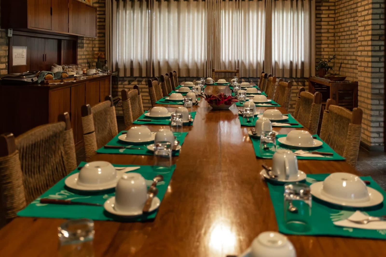 Pension complète, table bien mise, et les zones humides qui attendent juste dehors. Grande table en bois dressée pour un groupe avec des coupelles blanches, des sets de table verts et des chaises tressées dans la salle à manger en brique d'un lodge de safari dans le Pantanal Sud