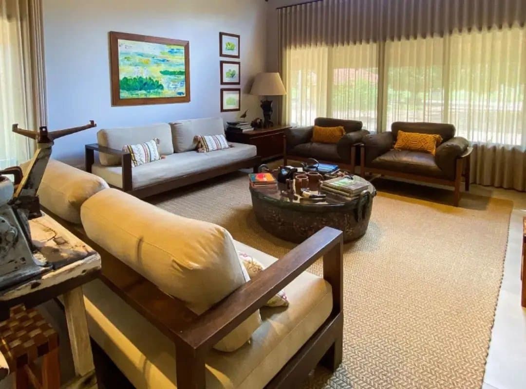 Des livres de terrain, des coussins chauds et la nature juste derrière les rideaux. Salon confortable d'un lodge de safari dans le sud du Pantanal, avec des canapés en bois sombre, une table basse ronde ancienne chargée de guides naturalistes, des tableaux de paysages colorés au mur et de larges fenêtres donnant sur la végétation
