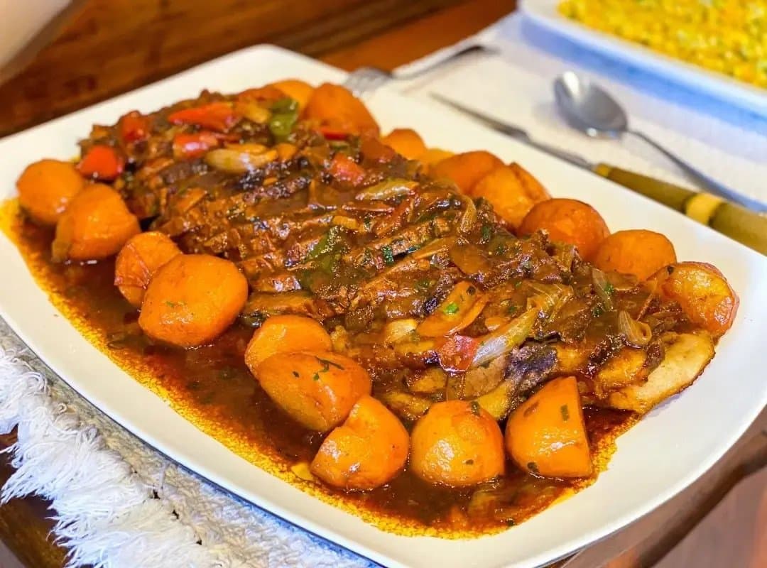 Un plat généreux qui rappelle que la cuisine du Pantanal ne fait pas dans la demi-mesure. Un grand plat de service blanc garni de bœuf braisé lentement dans une sauce foncée et riche, accompagné de pommes de terre rôties en boules, de poivrons et d'oignons sautés, servi dans un lodge de safari du sud du Pantanal