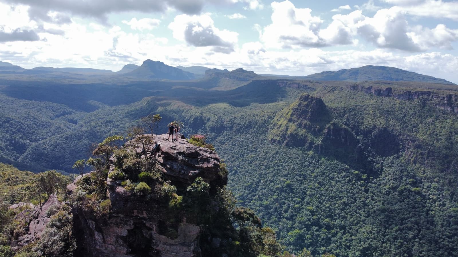 Den Aufstieg spürt man noch in den Beinen, den Ausblick noch länger. Photo: Alex Hubin Zwei Wanderer stehen auf einem bemoostem Sandsteinfelsen beim Chapada-Diamantina-Trek, mit tiefen bewaldeten Schluchten und gestuften Tafelbergen bis zum Horizont unter teils bewölktem Himmel