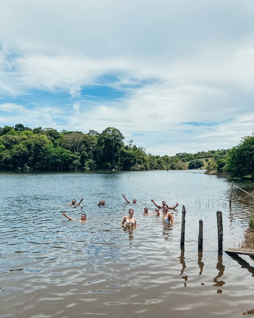 Pedalada longa, mergulho rápido, sorriso garantido. Um grupo de ciclistas nada e acena em um lago tranquilo cercado por mata fechada durante um passeio de ciclismo na Bahia