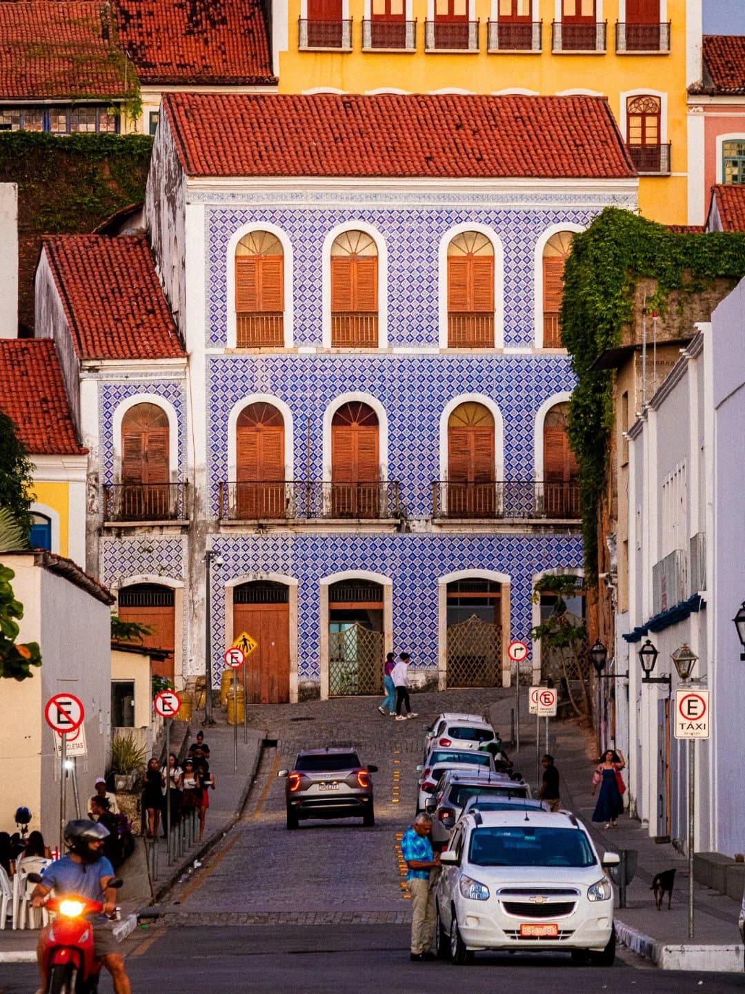 Une façade couverte d'azulejos qui arrête les passants depuis des siècles. Bâtiment colonial de trois étages recouvert d'azulejos portugais bleu et blanc sur une rue pavée de Santo Amaro, avec des façades colorées voisines et des habitants en pleine journée sous la lumière dorée