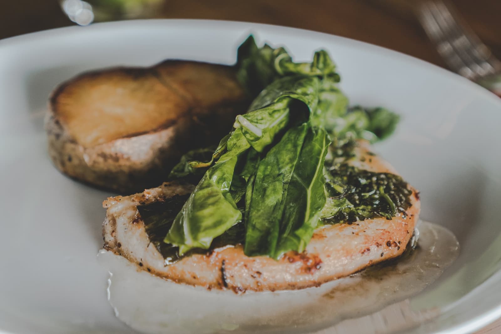 Pas de chichis, juste du bon. La cuisine de lodge à son meilleur. Filet de poisson poêlé garni de feuilles vertes fraîches et d'un champignon portobello rôti servi dans une assiette blanche au Mirante do Gavião