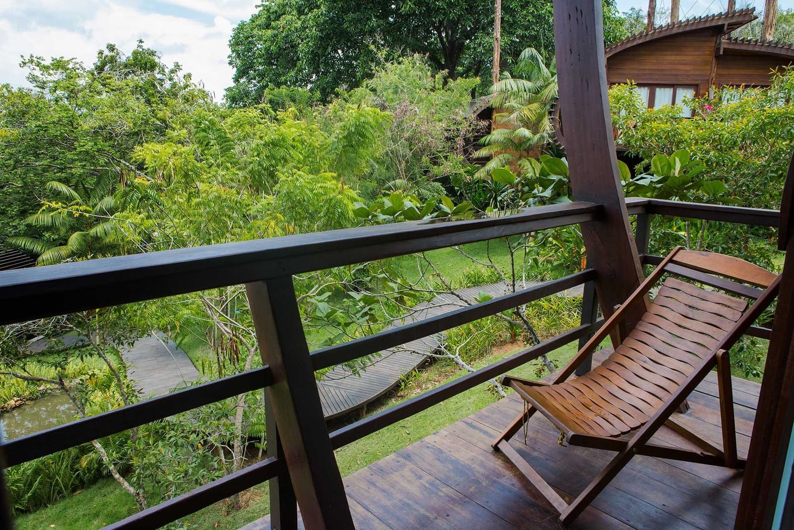 Le genre de terrasse qu'on ne quitte pas facilement. Une chaise longue en bois sur le balcon en terrasse du Mirante do Gavião, face à un jardin tropical luxuriant avec passerelle en bois et bungalow voisin