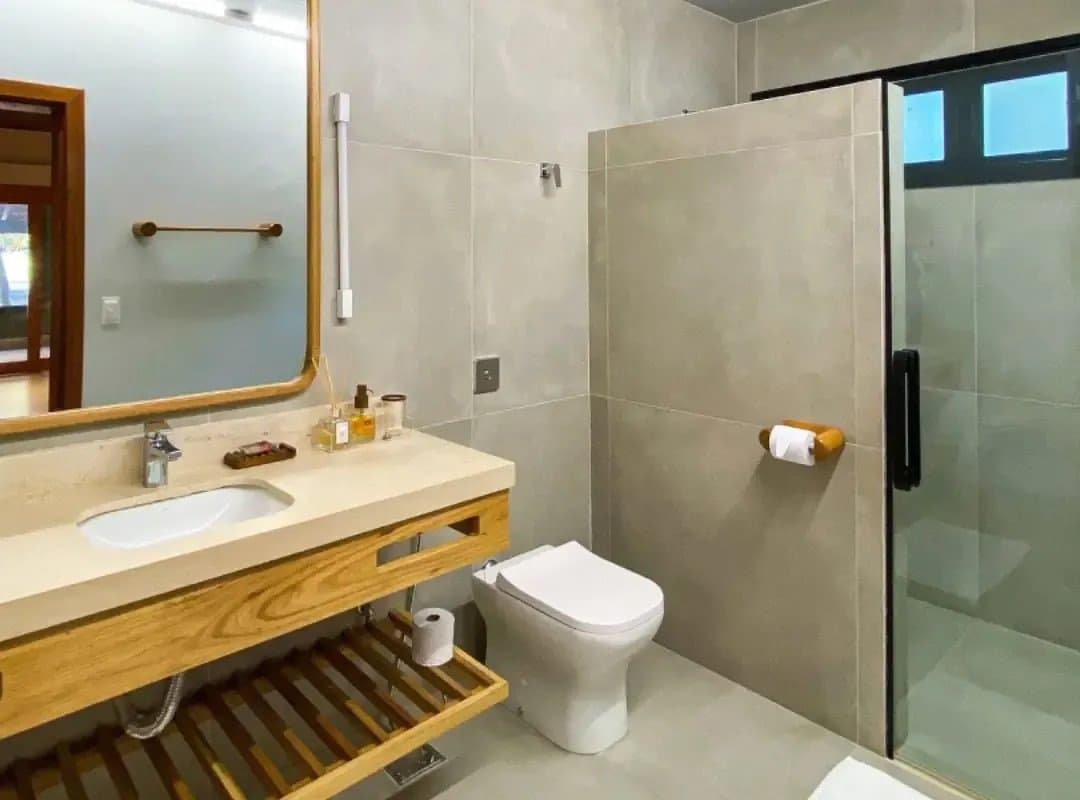Eau chaude, bois naturel, produits de toilette soignés. Le confort suit jusque dans les terres. Salle de bain moderne d'un lodge de safari dans le sud du Pantanal, avec meuble vasque en bois chaud, plan de travail en pierre, grand miroir et douche en verre sur carrelage neutre