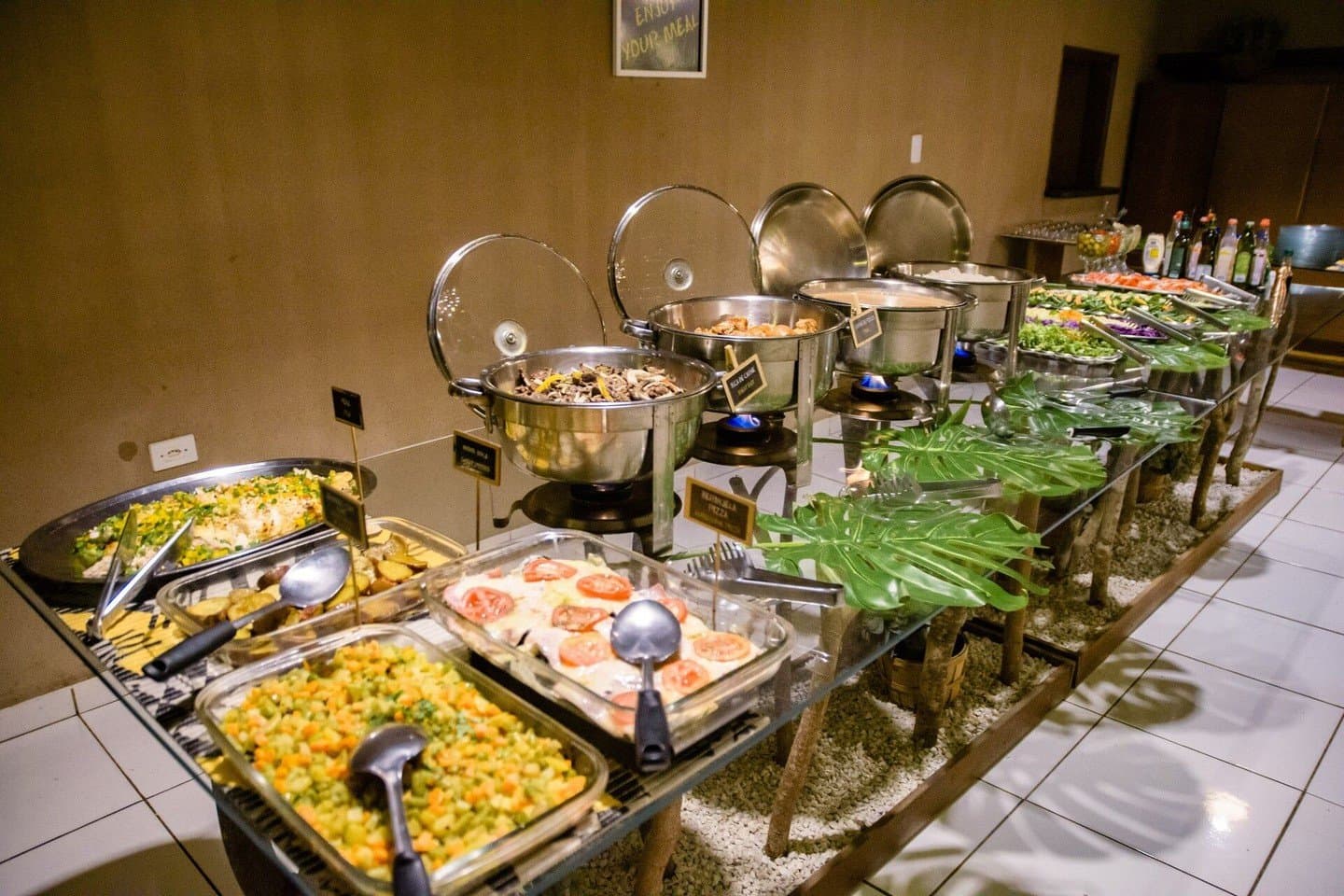 Nach dem Pirschgang wartet ein reichhaltiges Abendessen auf Sie. Ein langer Buffettisch in einer preiswerten Pantanal-Lodge mit Warmhaltebehältern, einem Auflauf mit Tomaten, gehacktem Gemüsesalat, grünen Salaten und tropischen Blattdekorationen