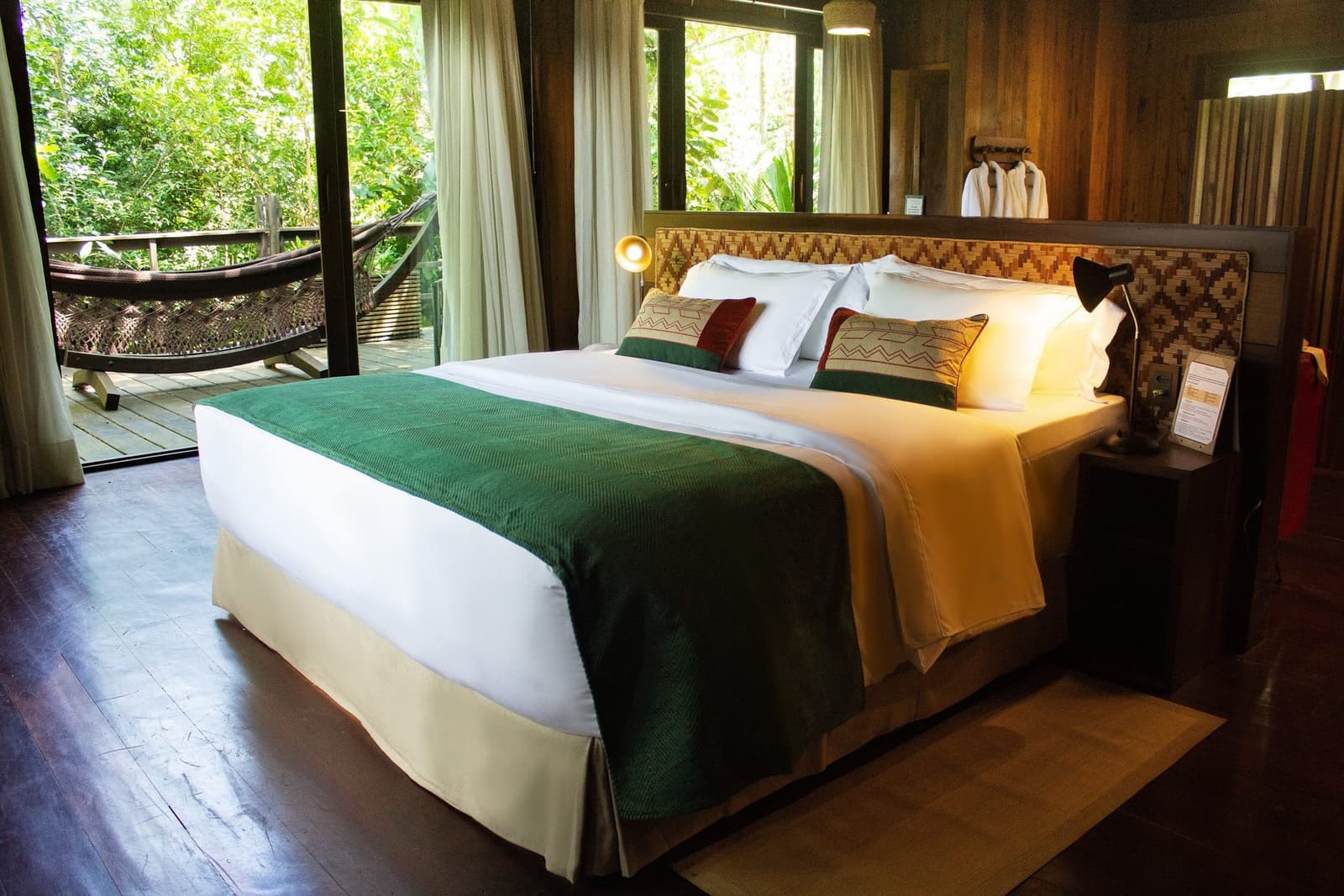 Le genre de chambre où l'on hésite à sortir du lit, jusqu'à ce qu'on entende les perroquets. Un grand lit avec une tête de lit tissée aux motifs géométriques et un chemin de lit en velours vert dans une chambre aux murs en bois du Mirante do Gavião, avec des portes vitrées ouvrant sur une terrasse privée dotée d'un hamac dominant la canopée