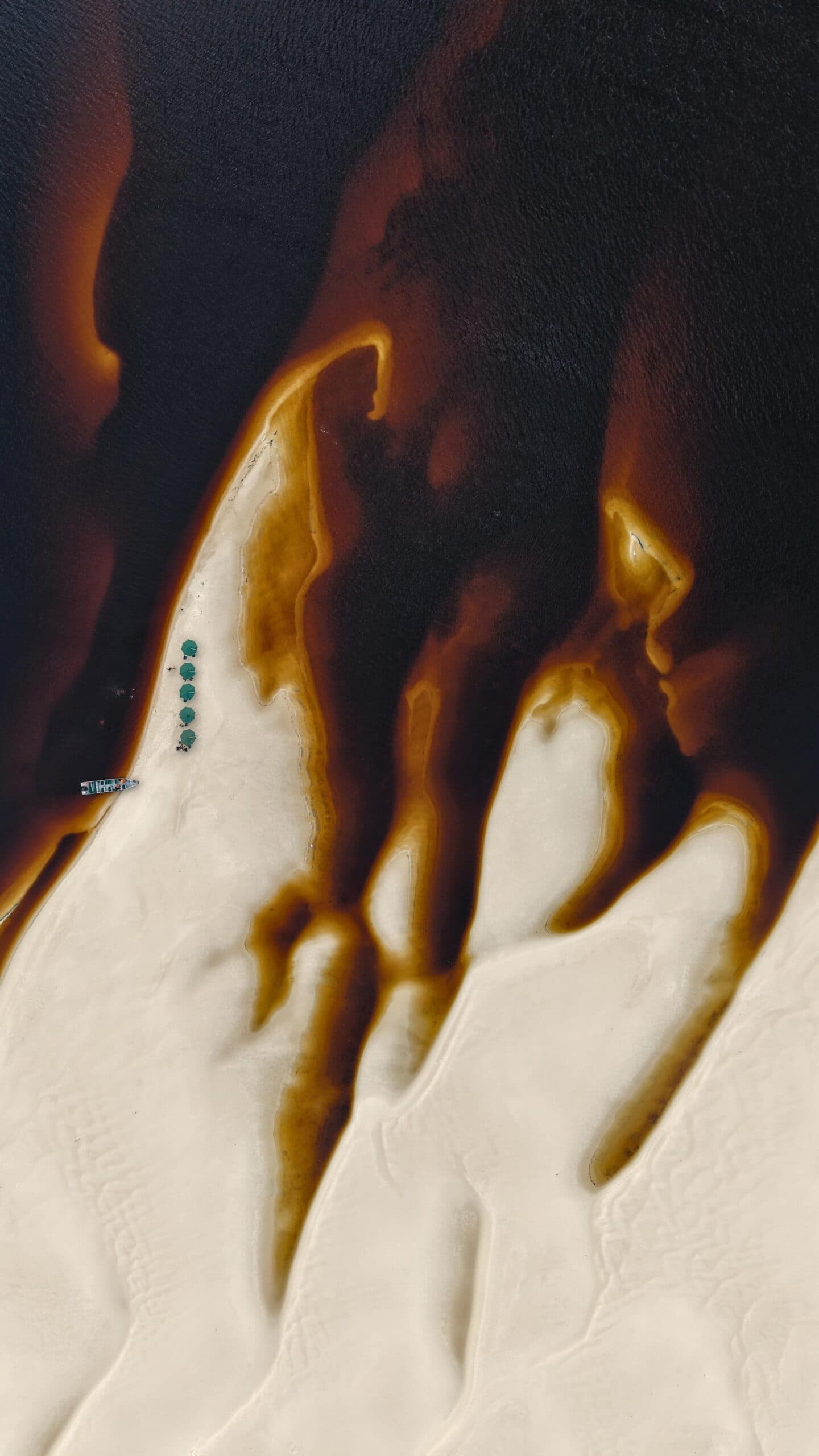 Vu d'en haut, le fleuve trace ses propres contours. Vue aérienne d'un banc de sable blanc se découpant dans les eaux sombres et tanniques du Rio Negro lors d'une croisière sur le fleuve Amazone au Brésil, avec un petit bateau fluvial et des parasols verts visibles depuis le ciel