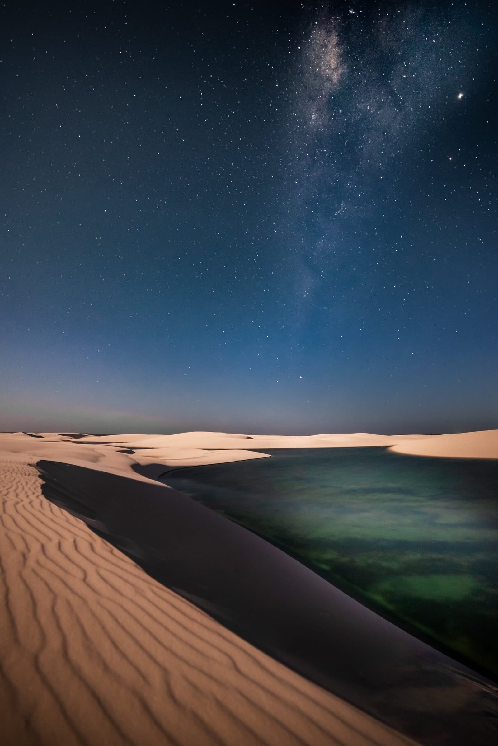 Noite sem lua, dunas sem fim, e o céu que parece perto demais. A Via Láctea em arco sobre dunas de areia branca e uma lagoa turquesa tranquila à noite no roteiro completo dos Lençóis Maranhenses