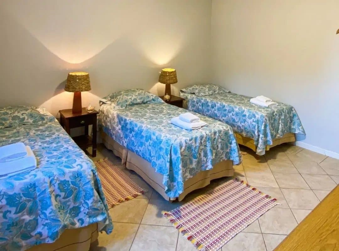 Sobre et accueillante, juste ce qu'il faut après une journée dans les plaines. Trois lits simples avec couvre-lits à fleurs bleues, serviettes pliées, abat-jours tressés et tapis colorés sur un sol carrelé dans une chambre de lodge de safari dans le sud du Pantanal