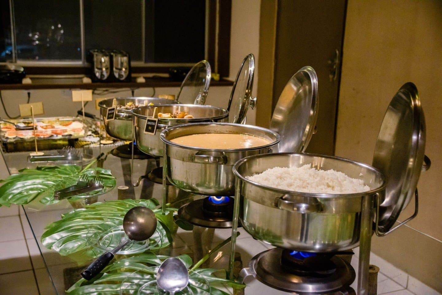 Warmes Essen, blaue Flammen, nach einem langen Tag draußen genau das Richtige. Edelstahl-Chafing-Dishes mit Reis und einer warmen Soße, die über blauen Flammen heiß gehalten werden, beim Abendessen-Buffet einer Lodge im Pantanal