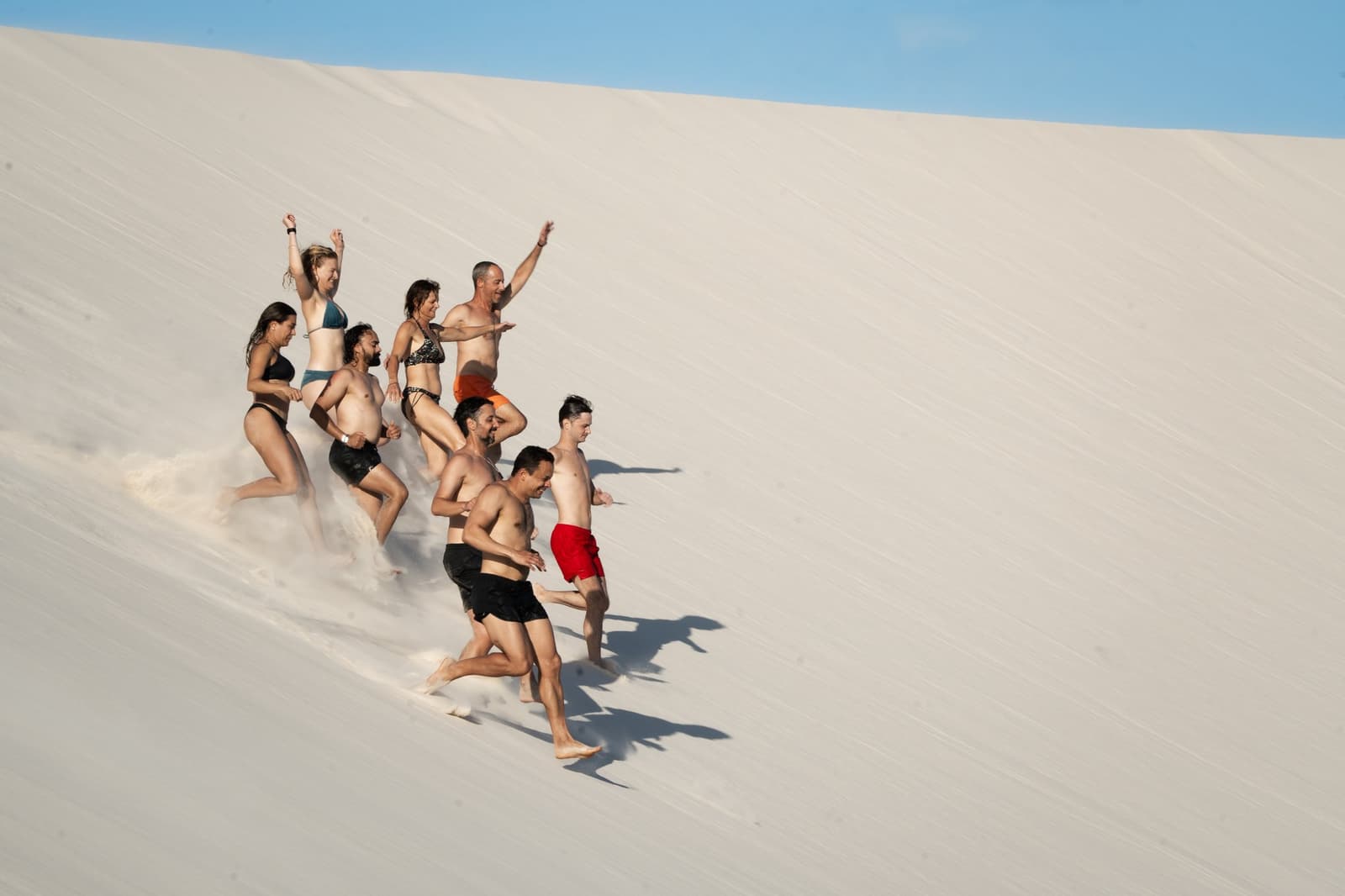 Descer a duna correndo é, digamos, parte obrigatória do roteiro. Um grupo de oito viajantes de roupa de banho corre e ri descendo uma duna de areia branca íngreme durante o trek pelos Lençóis Maranhenses saindo de Atins, com braços erguidos e areia voando sob os pés.