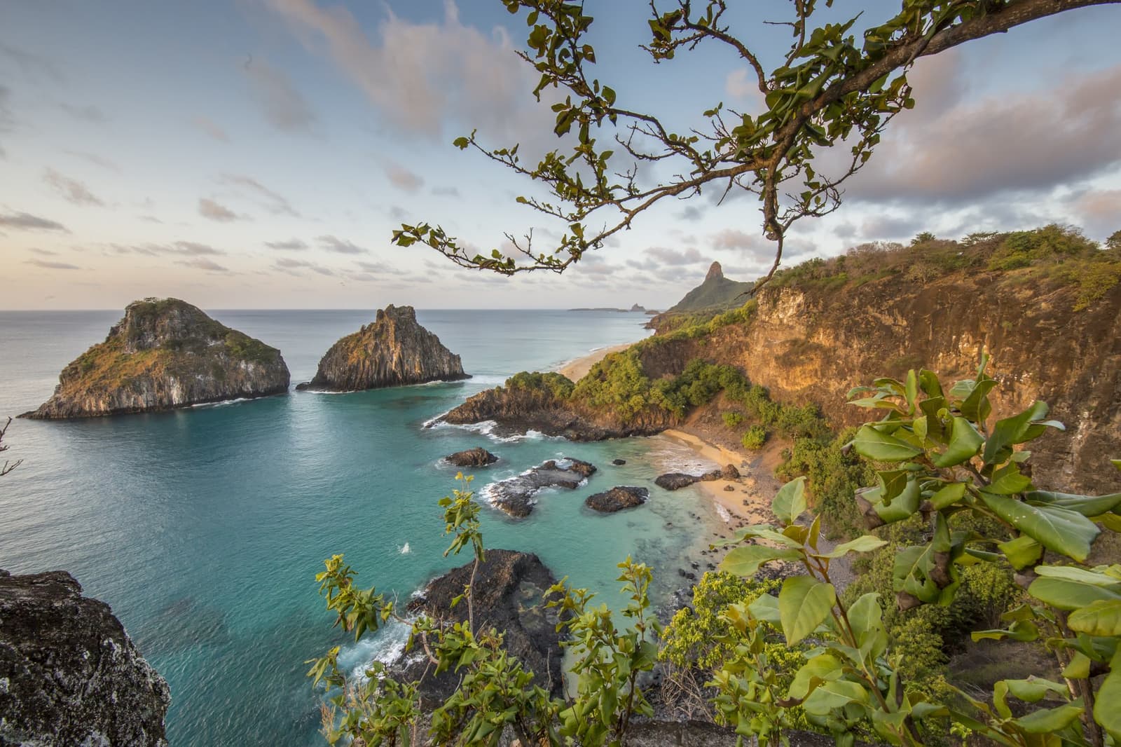 Vanaf hier snap je meteen waarom niemand meer naar huis wil. Panoramisch uitzicht op turquoise baaien, gouden kliffen en twee markante rotseilandjes aan de kust van Fernando de Noronha