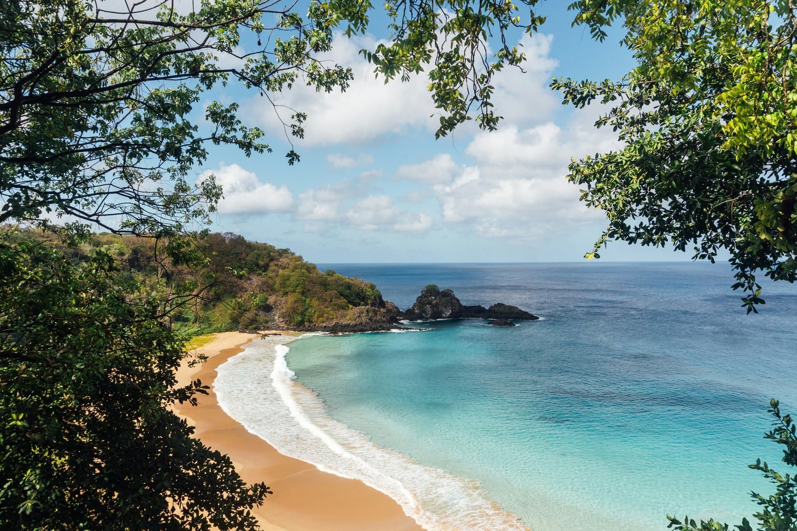 Durch das Blätterdach lugen, und plötzlich fehlen einem die Worte. Eine abgelegene Bucht mit goldenem Sand, türkisfarbenem Wasser und vulkanischen Felsen, eingerahmt von tropischer Vegetation auf Fernando de Noronha