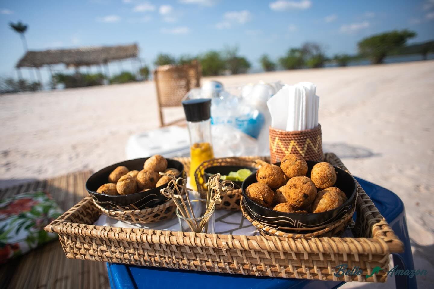 Un arrêt sur banc de sable, et l'Amazonie sort le plateau d'apéro. Un plateau en rotin tressé portant deux bols noirs de boulettes frites dorées, servis sur une plage de sable lors d'une croisière sur l'Amazone depuis Alter do Chão, accompagnés de piques en bambou, de quartiers de citron vert et de condiments
