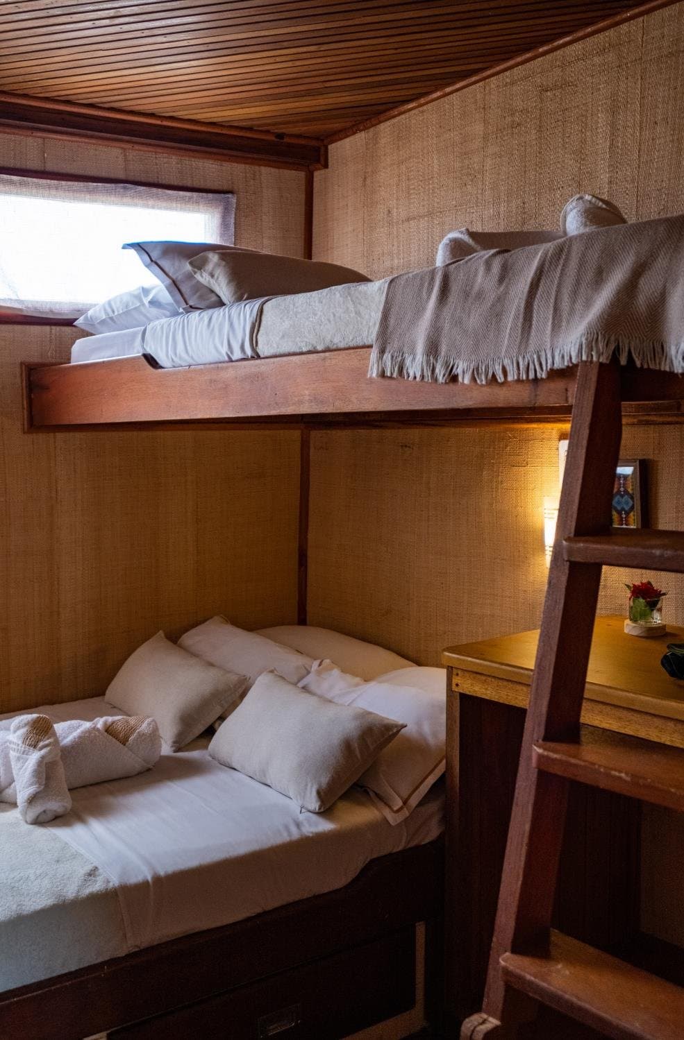 Petit espace, grand confort, le fleuve fait le reste du travail. Cabine en bois avec lits superposés à bord d'une croisière sur l'Amazone au départ d'Alter do Chão, avec linge blanc, coussins moelleux, un jeté à franges sur la couchette haute et un éclairage tamisé