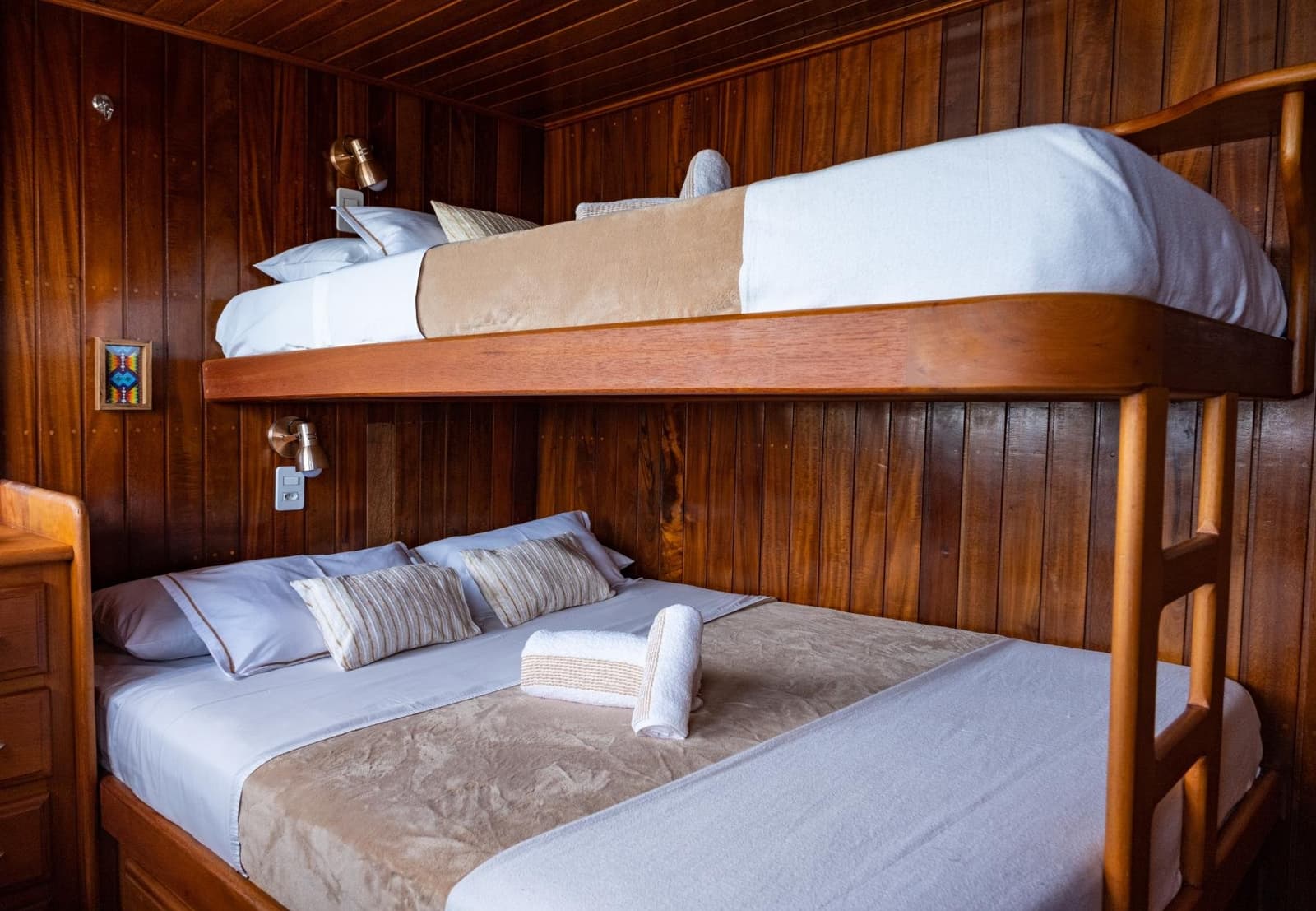 Petite, chaleureuse, et le fleuve s'occupe du reste. Une cabine en bois poli avec lits superposés à bord d'une croisière sur l'Amazone depuis Alter do Chão, avec une couchette double inférieure habillée de linge blanc et taupe, une couchette supérieure, des lampes de lecture en laiton et des lambris en bois sombre