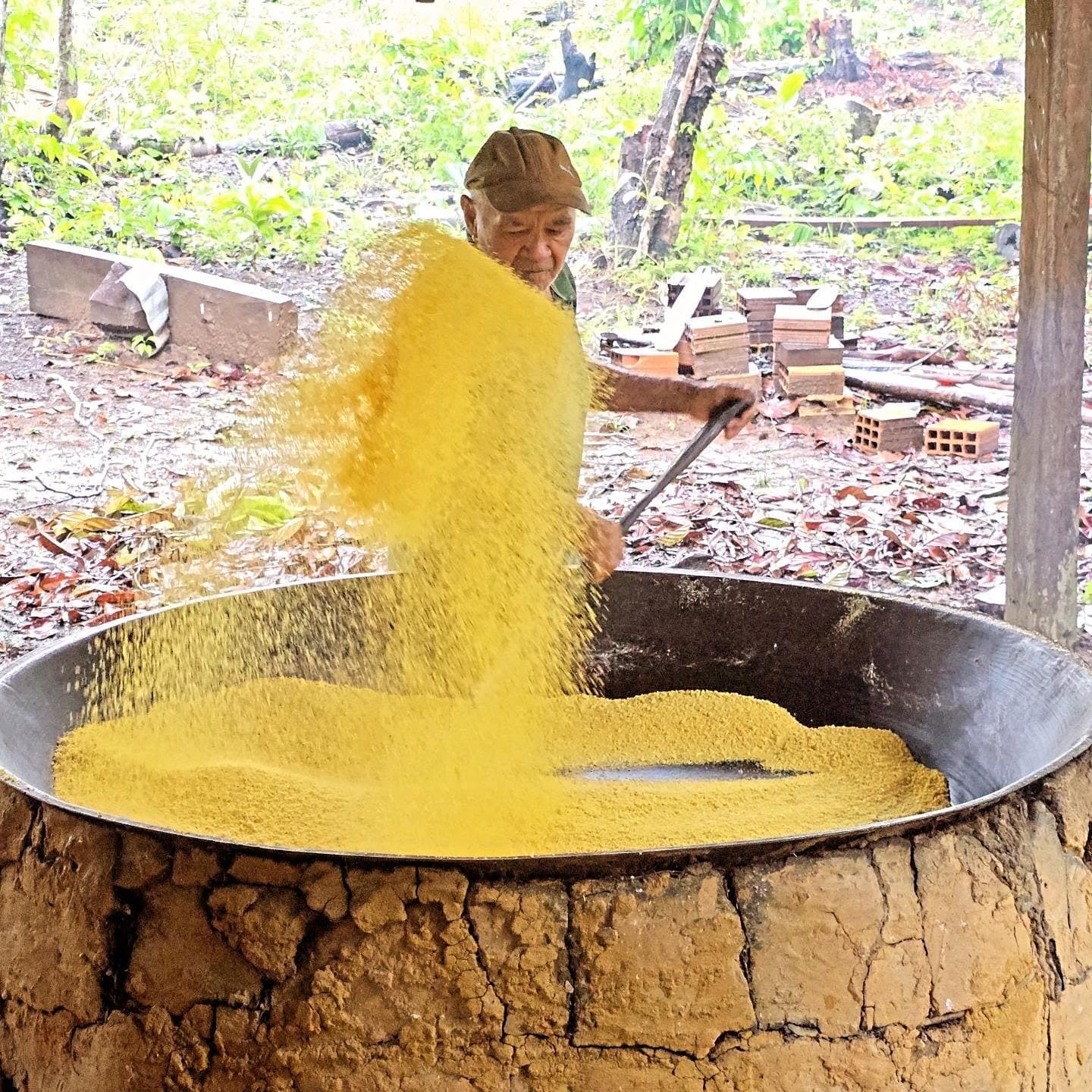La farinha façon ancienne: du bras, un grand chaudron, et rien de pressé. Un homme âgé fait griller de la farine de manioc dorée dans une grande poêle en fer sur un four en argile, lors d'une visite communautaire pendant une croisière sur l'Amazone depuis Alter do Chão