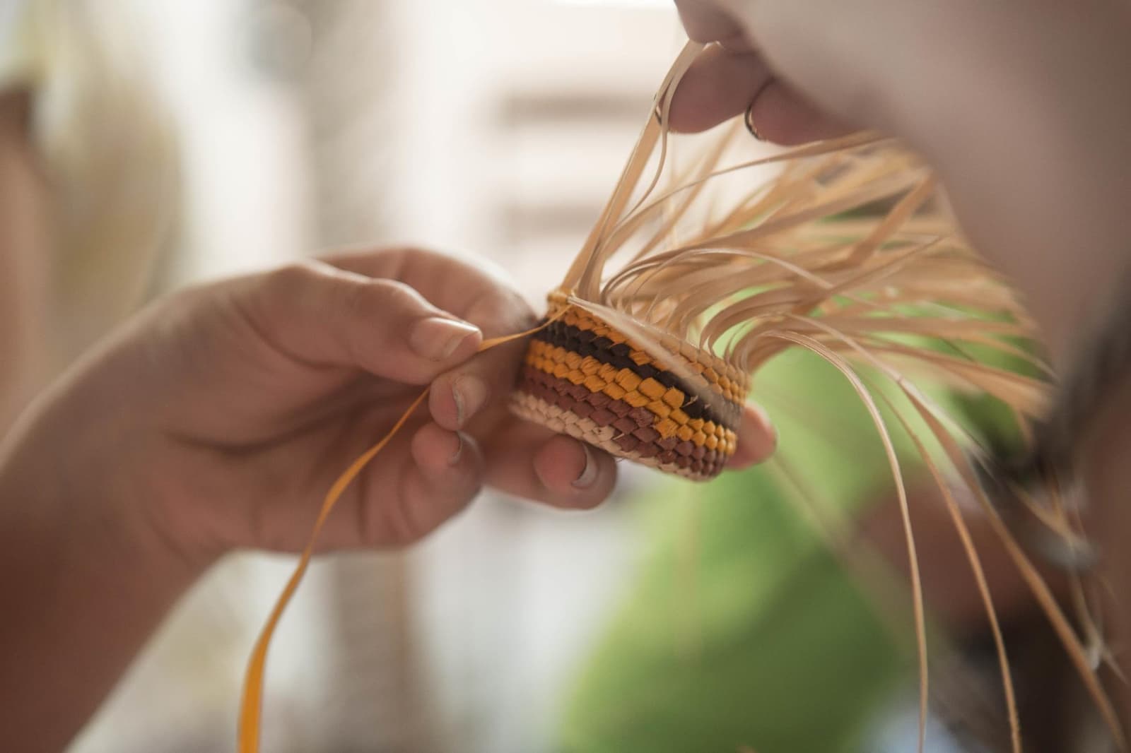 Un simple brin de fibre entre les mains, et soudain le temps change de rythme. Gros plan sur des mains tressant un petit panier rayé avec des fibres de palmier naturelles lors d'une croisière sur l'Amazone depuis Alter do Chão