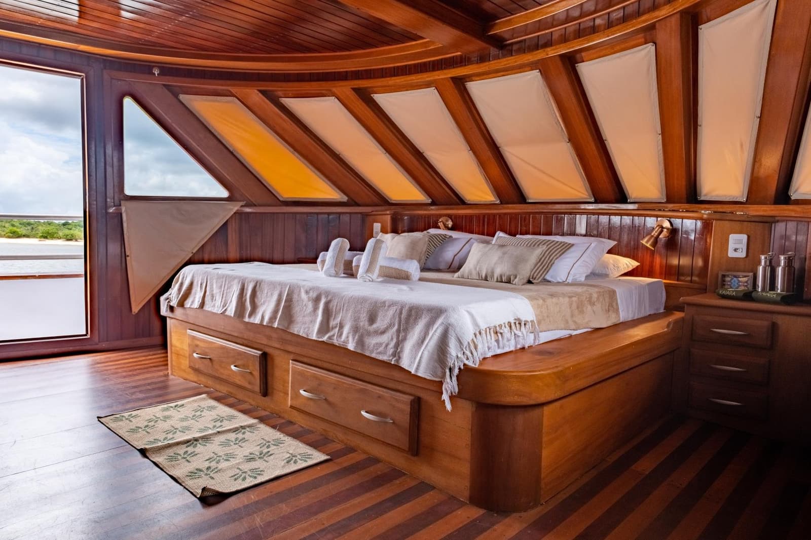 Le confort du bois, le fleuve juste à côté, c'est ça, dormir en Amazonie. Cabine principale en bois verni à bord d'une croisière sur l'Amazone au départ d'Alter do Chão, avec un lit double encastré, des tiroirs de rangement, des lucarnes en toile et une porte latérale ouverte sur le paysage fluvial