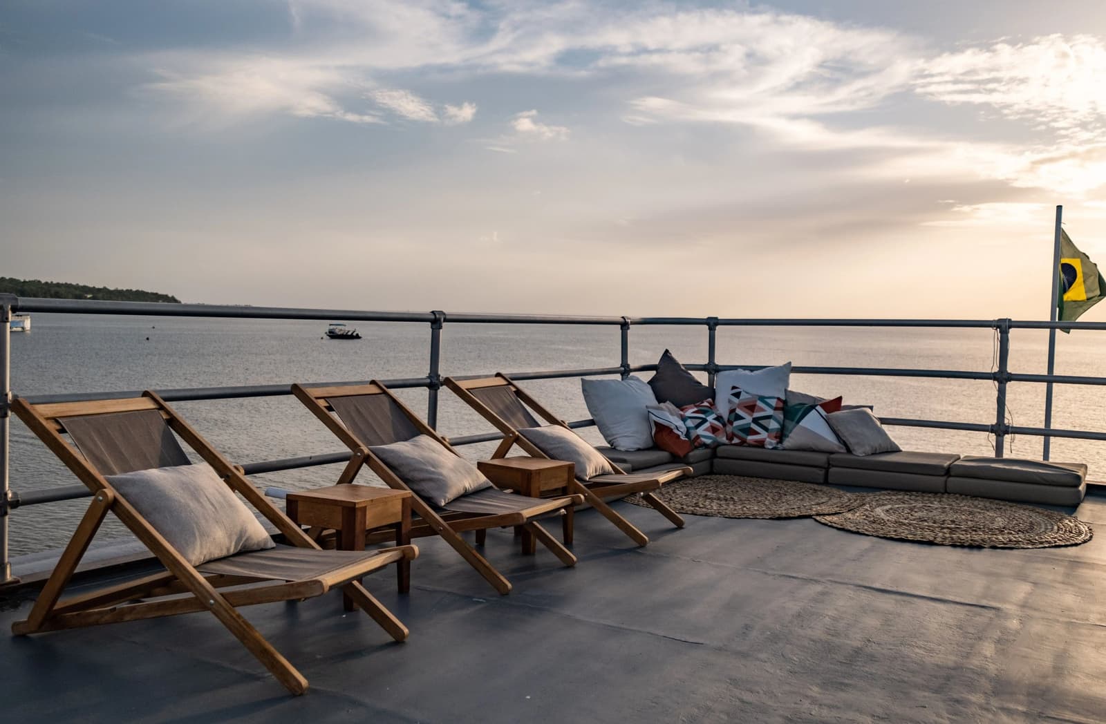Ce pont, ce fleuve, ce ciel. Difficile de rentrer à l'intérieur. Chaises longues en teck et coin salon rembourré sur le pont supérieur d'une croisière Amazon au départ d'Alter do Chão, avec un large fleuve s'étendant à l'horizon sous un ciel de fin de journée et le drapeau brésilien flottant à la poupe