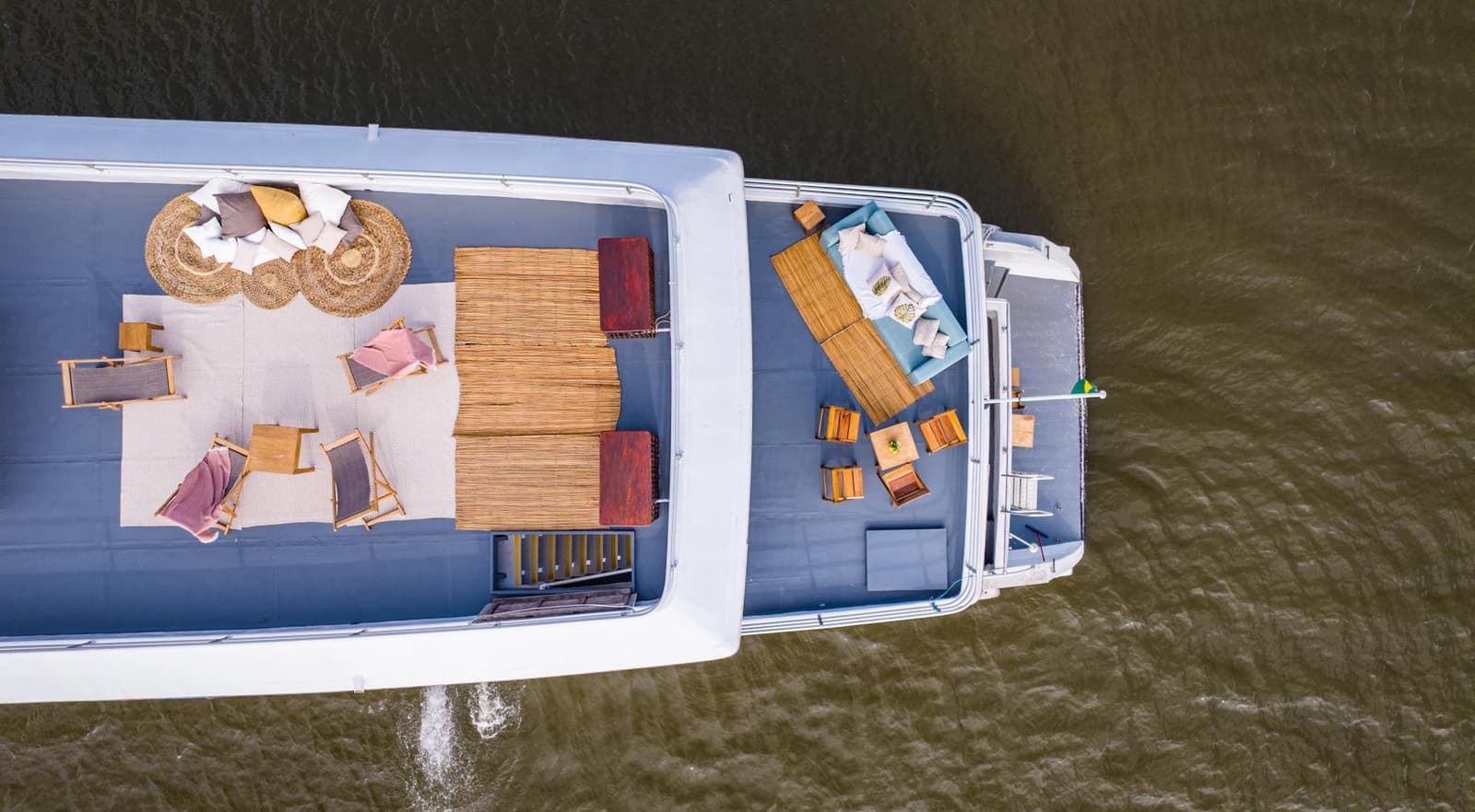 Un salon flottant, avec le fleuve comme unique voisin. Vue aérienne d'un bateau de croisière en Amazonie depuis Alter do Chão, avec deux ponts soleil aménagés de chaises longues en bois, tapis en rotin, abris en chaume et sièges rembourrés sur un large fleuve brun