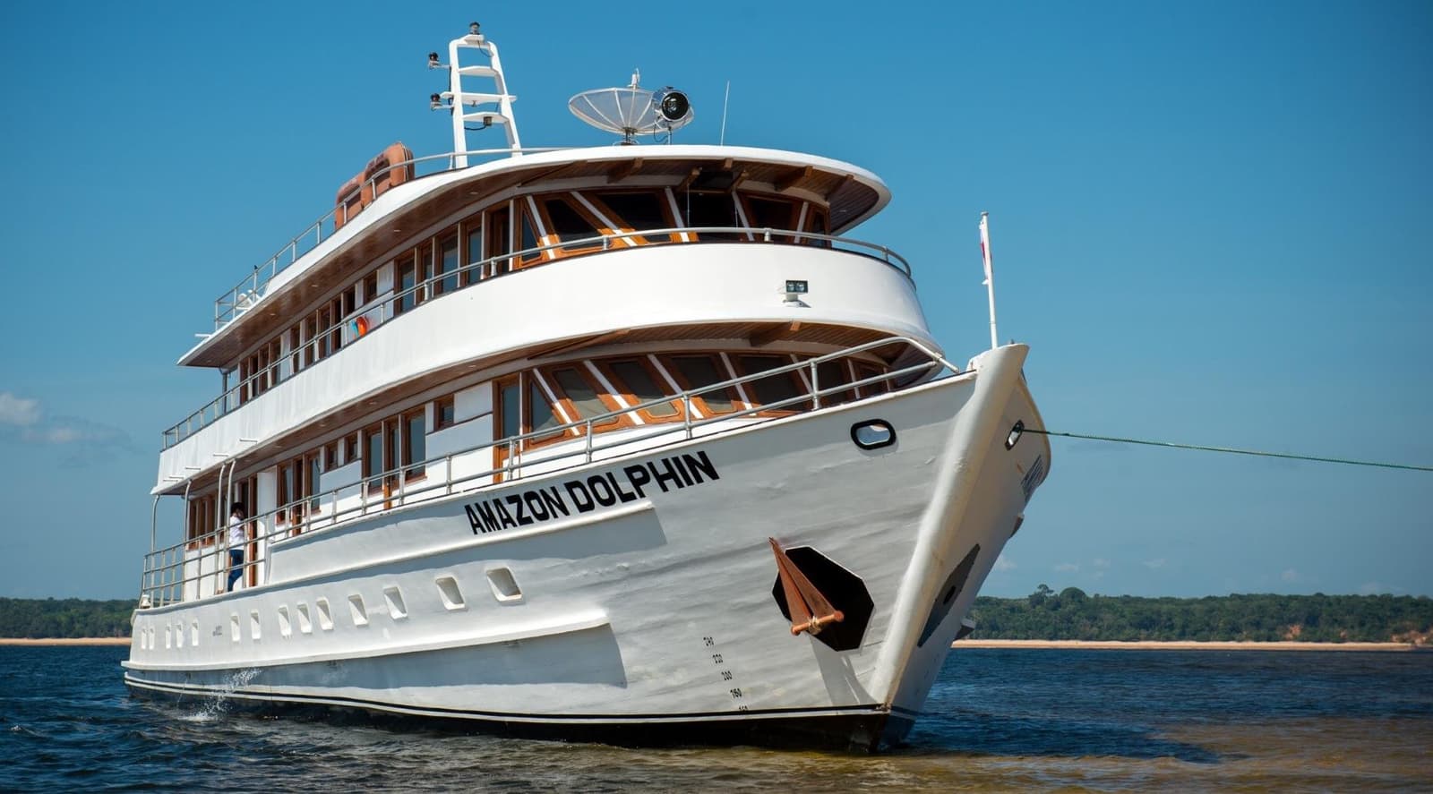 Un bateau à la hauteur du fleuve qui l'accueille. Le navire de croisière fluviale Amazon Dolphin, à plusieurs ponts avec une coque blanche et des garnitures en teck chaud, navigue sur un large chenal sous un ciel bleu éclatant — croisière en Amazonie au départ d'Alter do Chão