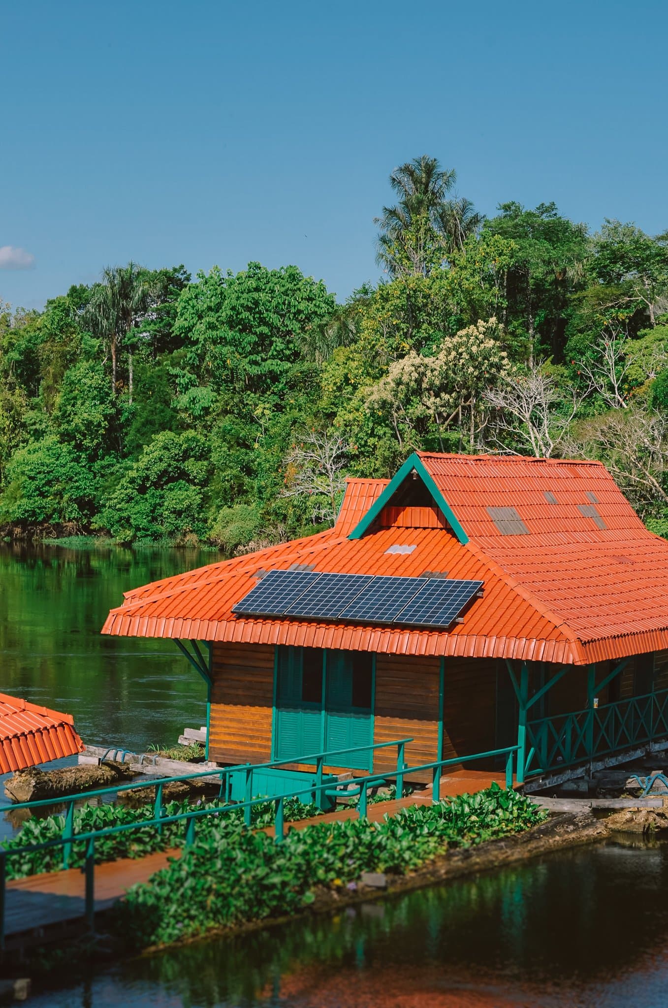 Solar, flutuante e no meio da floresta, a vida simples tem seus encantos. Uma cabana flutuante de madeira com telhado laranja e painel solar sobre um rio escuro em uma viagem de ecolodge na floresta amazônica no Brasil, com densa vegetação tropical ao fundo
