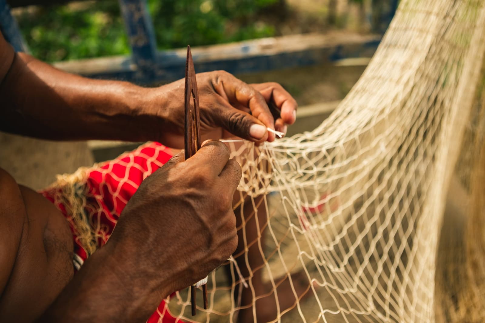 Nas mãos do ribeirinho, cada nó tem uma história. Close-up de mãos habilidosas usando uma agulha de madeira para remendar uma rede de pesca, artesanato tradicional das comunidades ribeirinhas da Amazônia