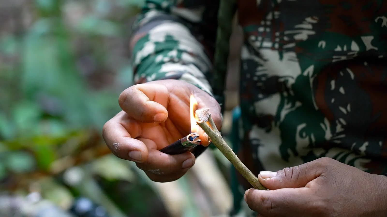 Uraltes Wissen, eine kleine Flamme, tiefer Wald. Ein Führer in Tarnkleidung entzündet mit einem Feuerzeug einen grünen Ast im Regenwald und demonstriert eine Buschcraft-Feuertechnik auf einer Amazon-Trek- und Survival-Tour