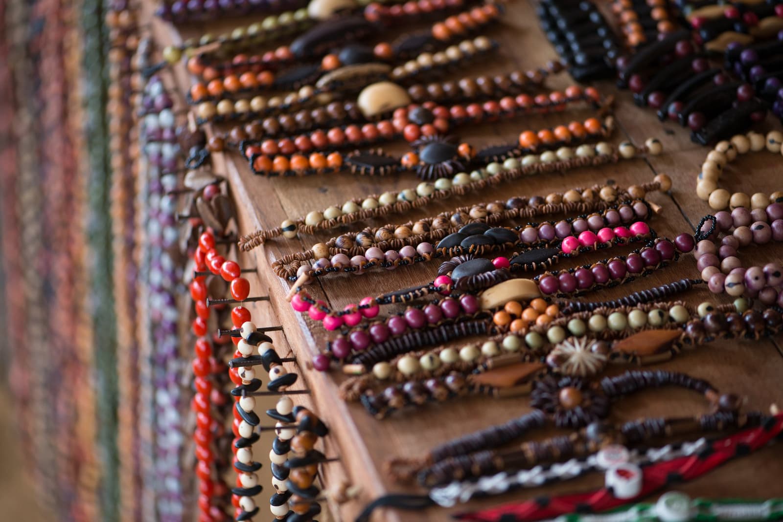 Sementes da floresta que viram lembrança nas mãos de quem sabe fazer. Fileiras de pulseiras artesanais com sementes naturais coloridas e contas de madeira expostas sobre uma tábua de madeira, confeccionadas por uma comunidade ribeirinha próxima à Anavilhanas Jungle Lodge Brasil