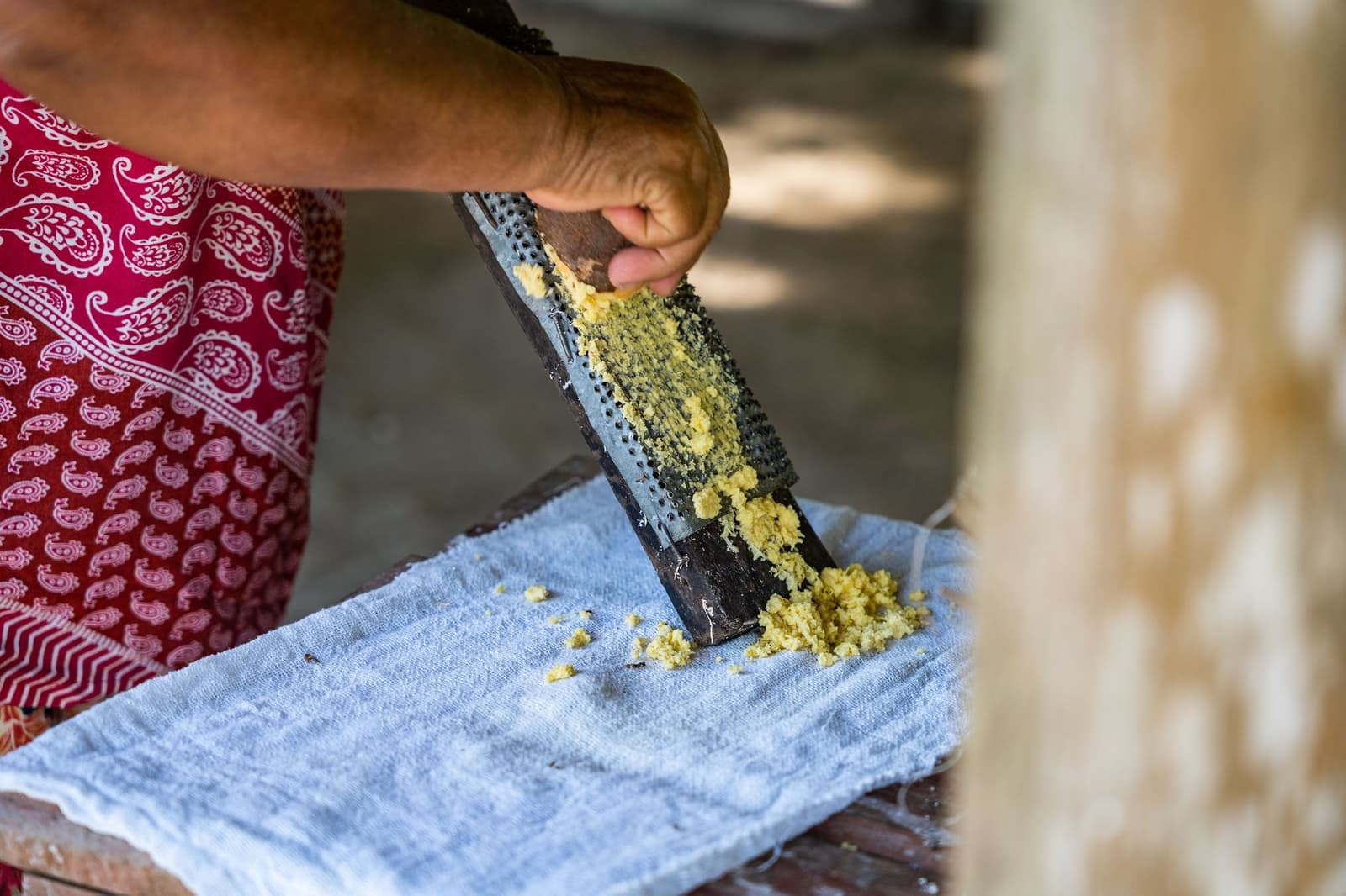 A farinha começa assim, no braço e no ritmo de sempre. Mulher com avental vermelho estampado rala mandioca fresca sobre um pano durante visita a comunidade ribeirinha próxima à Anavilhanas Jungle Lodge Brasil