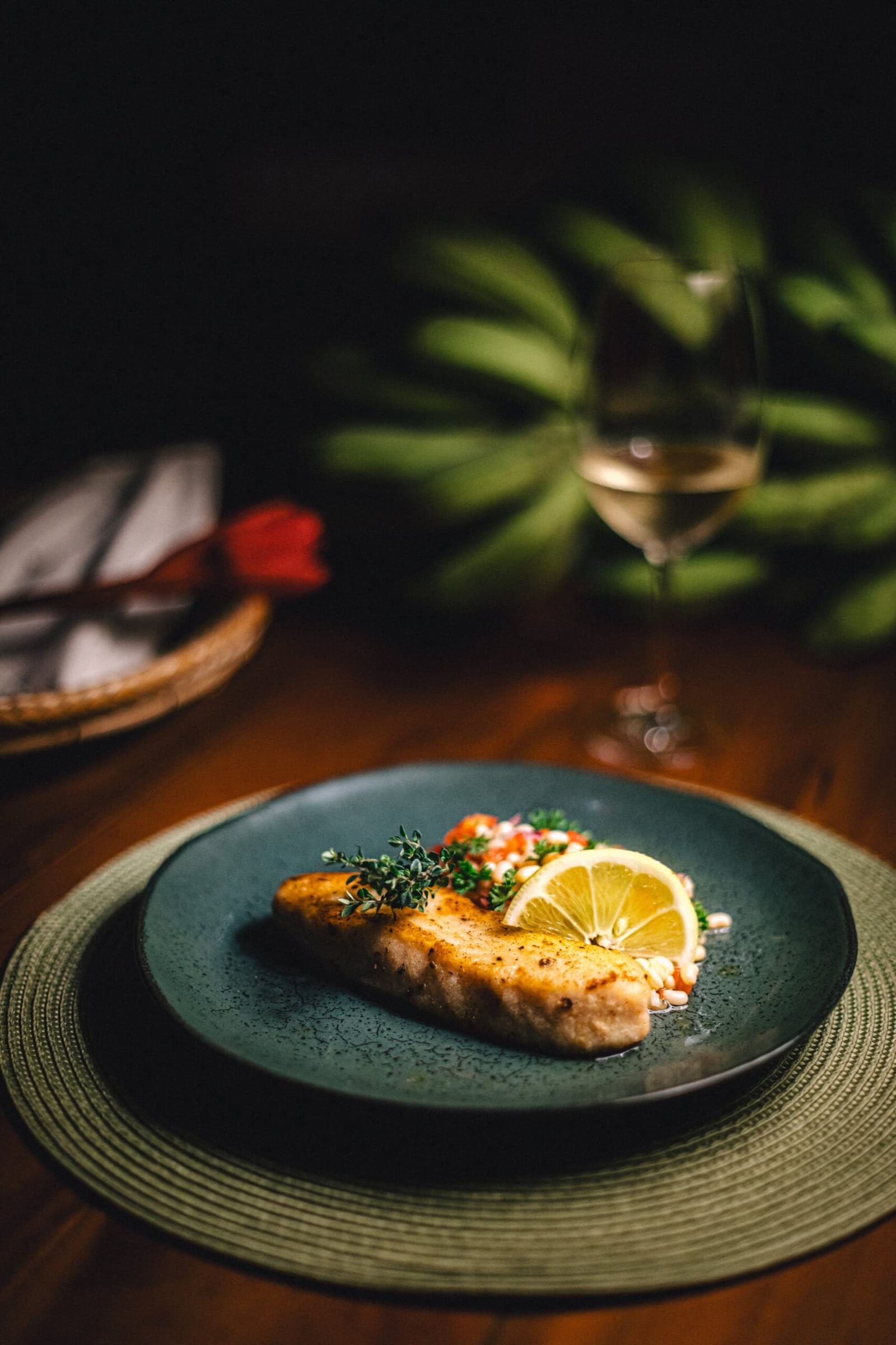 Cozinha cuidadosa, com a floresta amazônica como pano de fundo. Filé de peixe grelhado com ervas frescas e rodela de limão em prato de cerâmica escura no Anavilhanas Jungle Lodge Brasil, acompanhado de uma taça de vinho branco