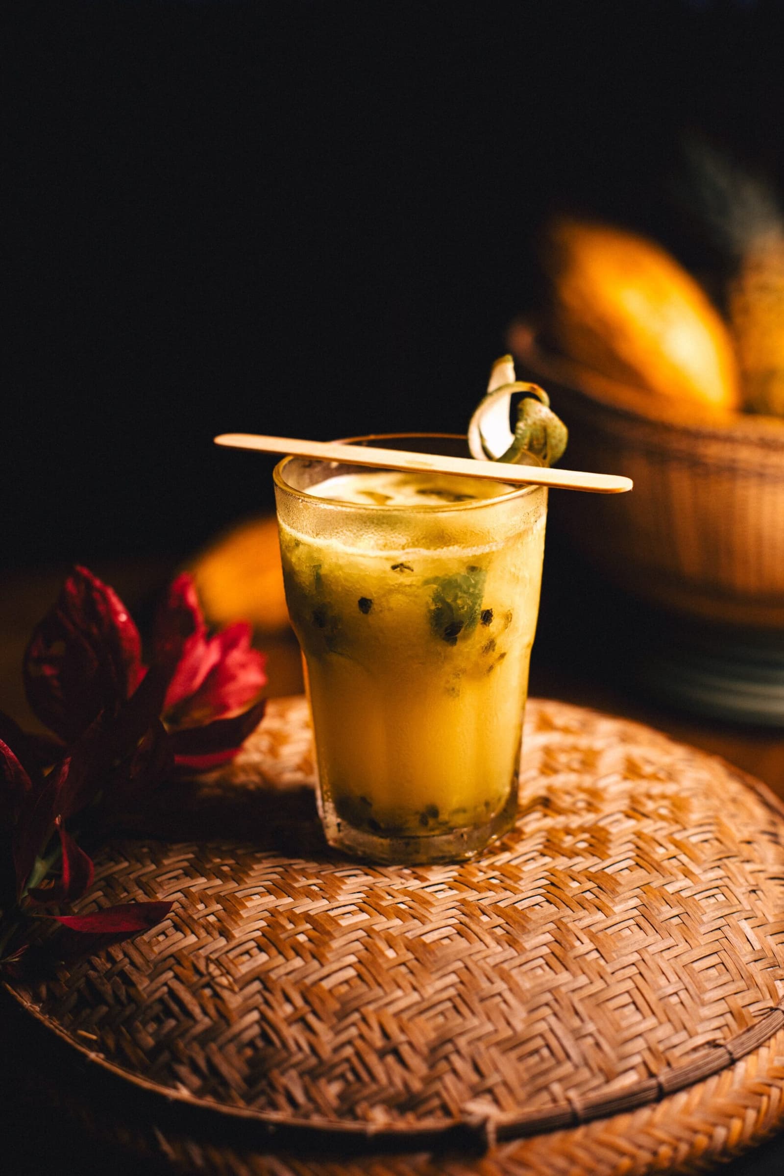 A maracujá chegou primeiro. A floresta vem logo depois. Um drinque dourado de maracujá com sementes visíveis servido em copo sobre uma bandeja de rattan trançado na Anavilhanas Jungle Lodge Brasil, decorado com um palito de madeira e uma folha tropical enrolada, com uma cesta de frutas amarelas ao fundo