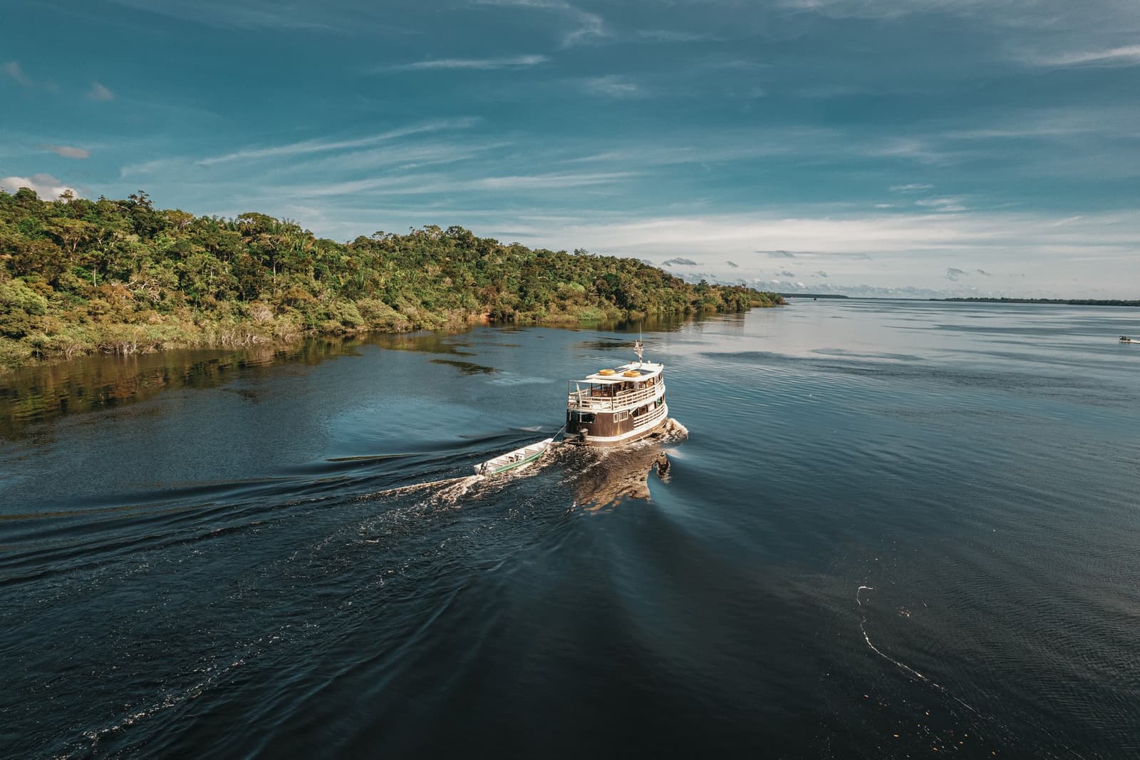O rio começa a revelar seus segredos assim que o barco ganha velocidade. Um barco regional de dois andares navega pelas águas escuras do Rio Negro ao longo de densa floresta amazônica em uma excursão de dia inteiro do Anavilhanas Jungle Lodge Brasil