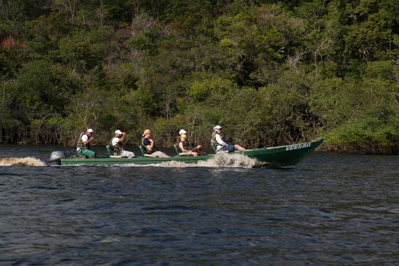 No rio, a floresta te lembra quem manda aqui. Um grupo de ecoturistas com coletes salva-vidas avança em alta velocidade pelo Rio Negro a bordo de um barco motor verde durante uma expedição do Anavilhanas Jungle Lodge Brazil, com densa mata ciliar na margem oposta
