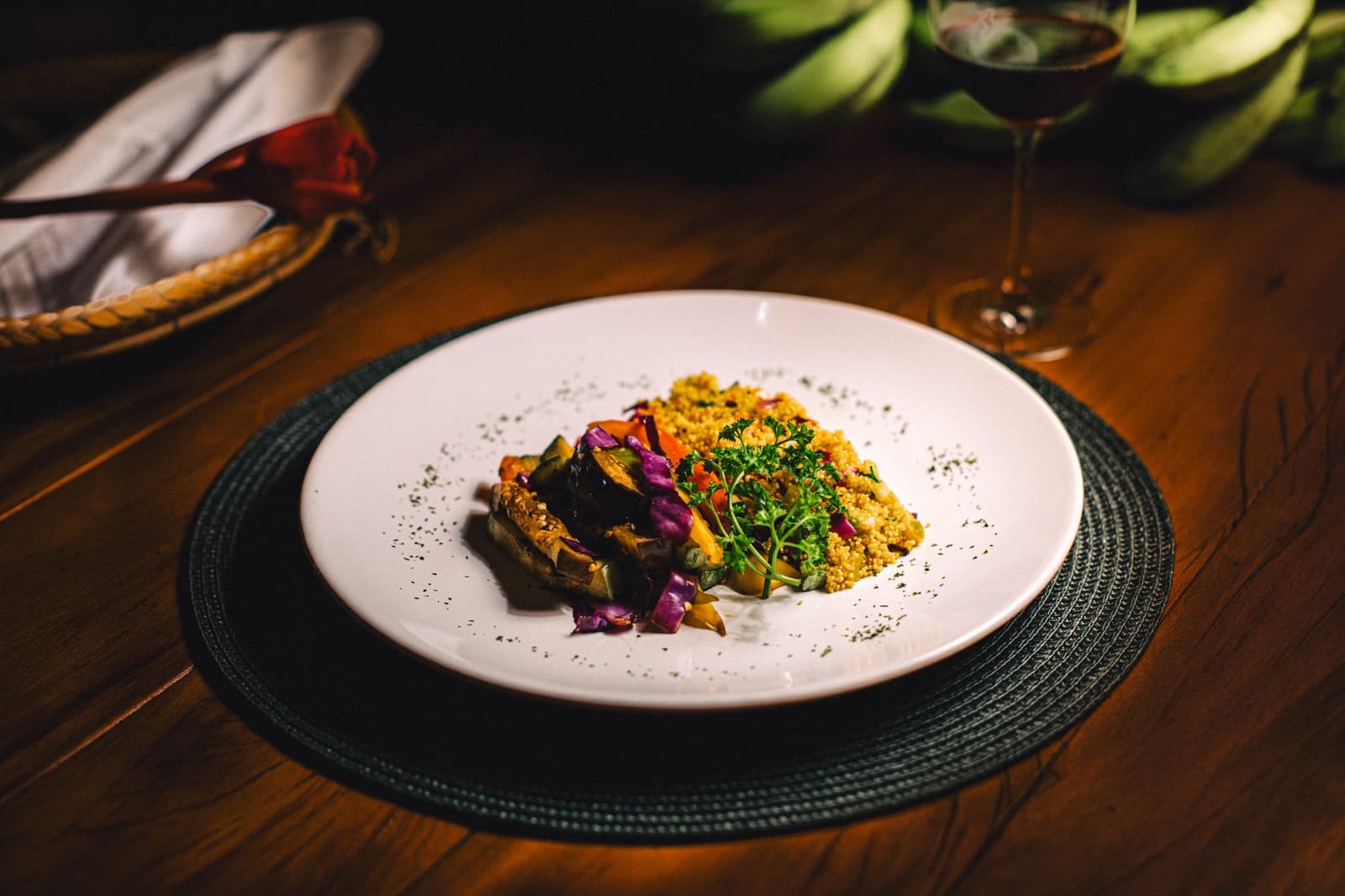Legumes coloridos, couscous quentinho e vinho tinto. O jantar na floresta tem suas vantagens. Prato de jantar no Anavilhanas Jungle Lodge com legumes assados, cuscuz dourado e ervas frescas em louça branca, com uma taça de vinho tinto ao fundo