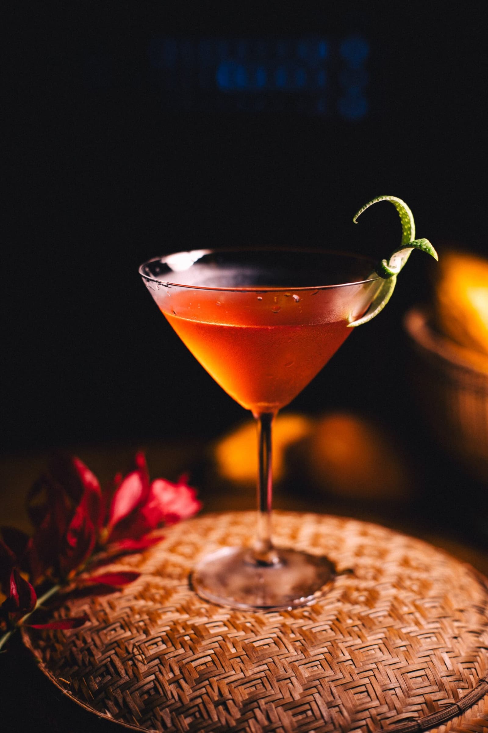 O fim do dia na floresta tem sabor próprio. Um coquetel vermelho intenso em taça martini com raspas de limão, apoiado em bandeja de palha ao lado de uma flor tropical vermelha no Anavilhanas Jungle Lodge Brasil