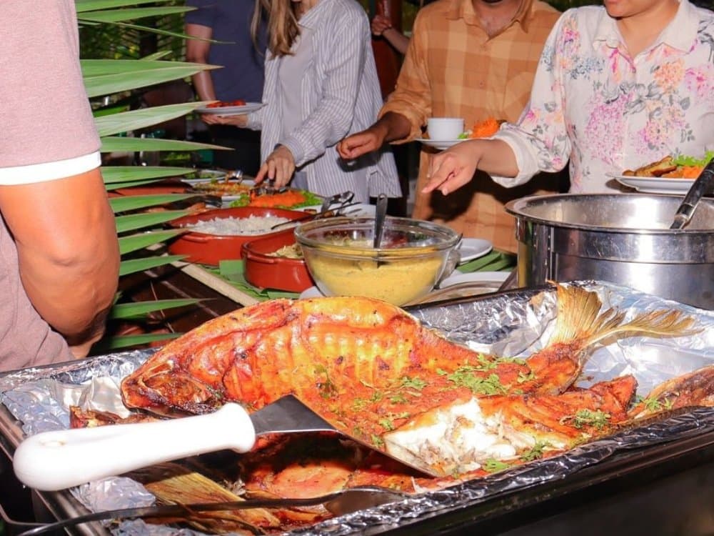 Recém-saído do rio, o peixe assado é a estrela do bufê na beira da floresta. Um peixe inteiro assado com ervas servido em uma assadeira de papel alumínio em um bufê ao ar livre durante um passeio pela selva amazônica brasileira, acompanhado de arroz, molho dourado e outros pratos enquanto os hóspedes se servem