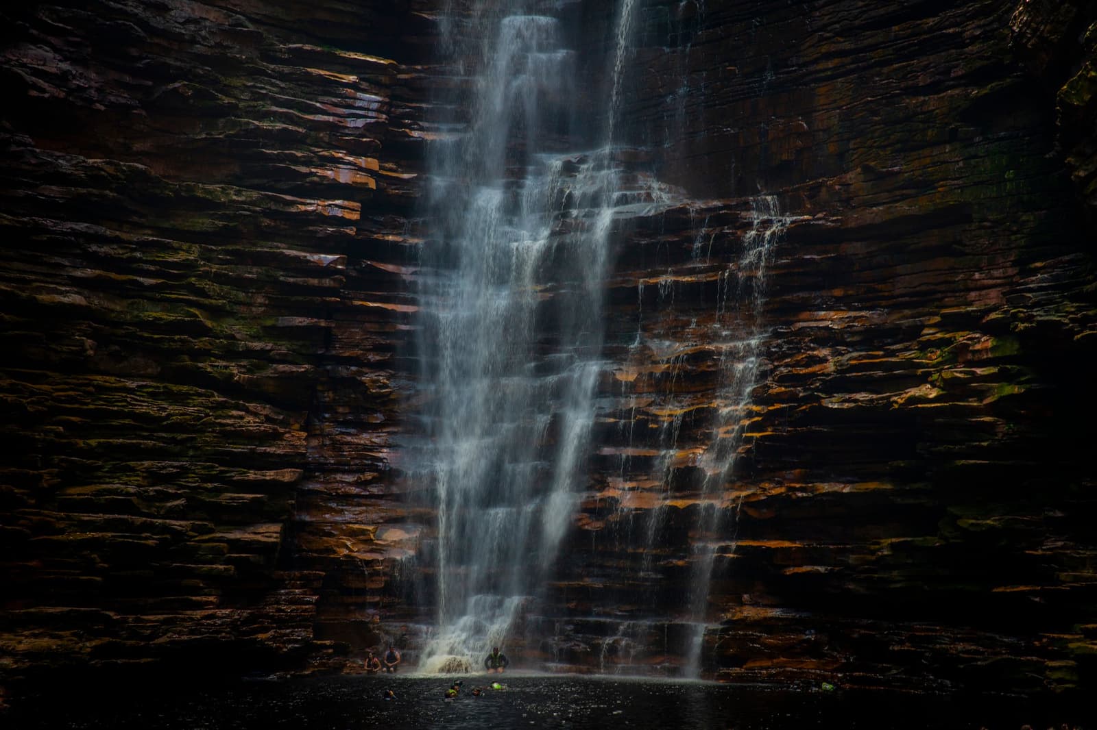 Un bassin naturel que l'on garde précieusement pour soi. Grande cascade étagée dévalant des falaises de grès en couches lors d'une randonnée dans la Chapada Diamantina, deux silhouettes minuscules visibles au bord du bassin
