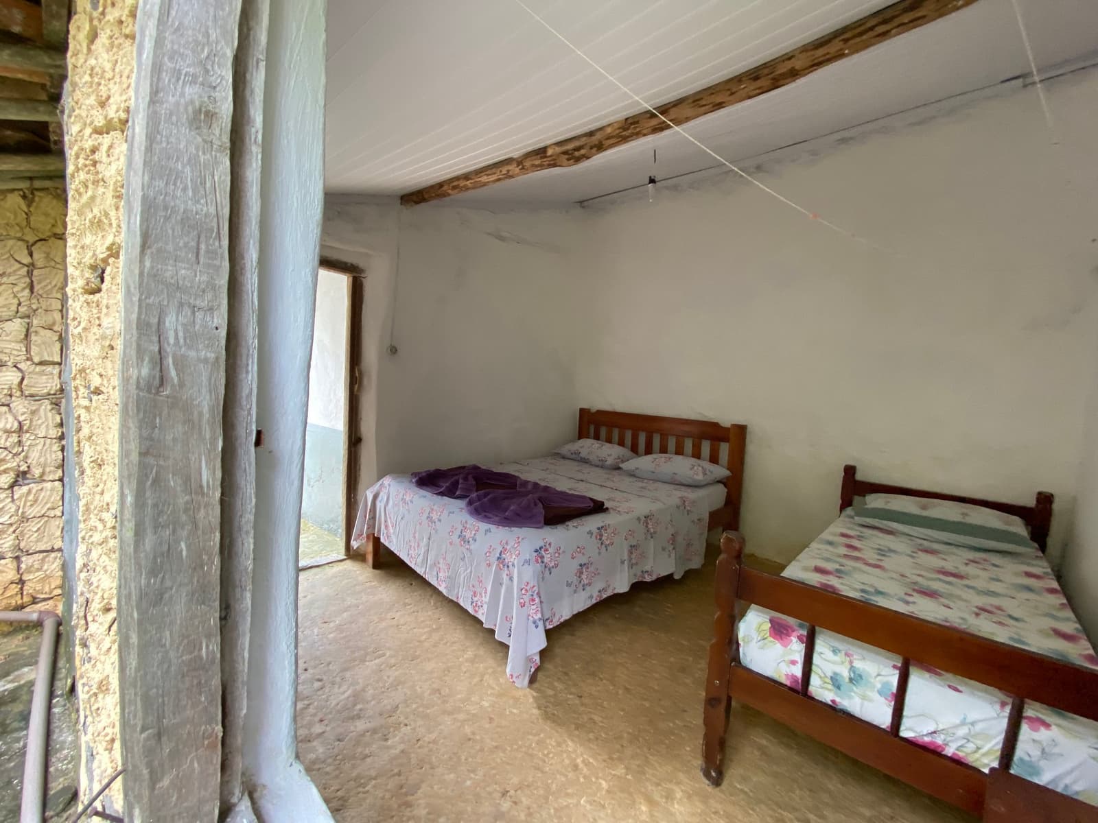 Sobre et sincère, comme il se doit après une journée de marche. Chambre simple avec deux lits en bois et parure de lit fleurie dans une pension rustique en pierre, typique des hébergements lors d'une randonnée dans la Chapada Diamantina