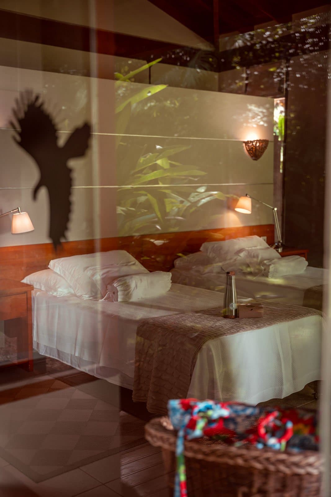 Het regenwoud klopt niet aan, het schuift gewoon mee naar binnen. Silhouet van een grote vogel geprojecteerd op de muur van een tweepersoonskamer in Cristalino Jungle Lodge, zichtbaar als reflectie in glas met warme bedlampen en tropisch gebladerte