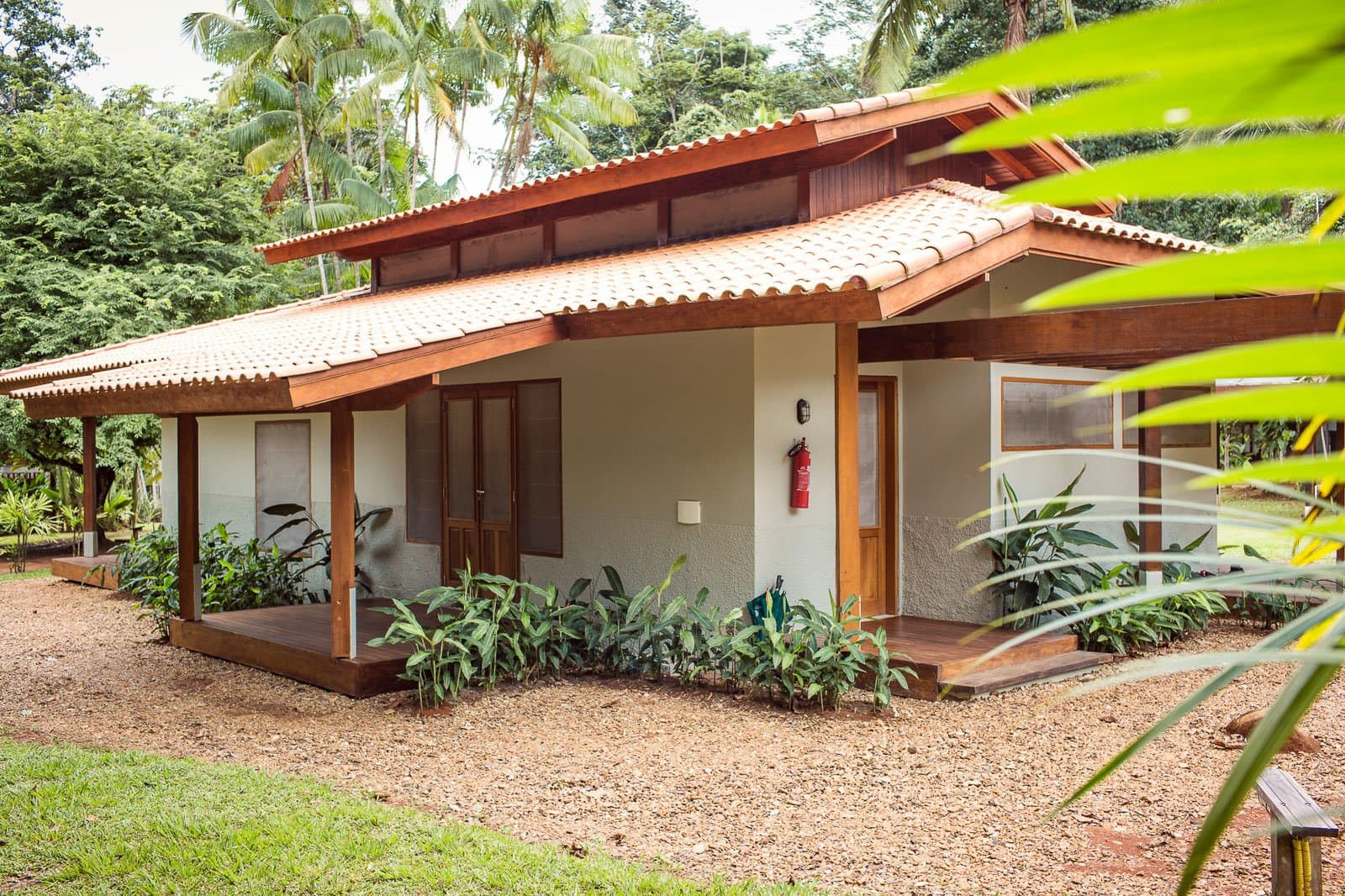 Klein van formaat, groot in sfeer, en het Amazonegebied begint achter de border. Buitenaanzicht van een chalet van Cristalino Jungle Lodge met terracotta pannendak, hardhouten veranda en weelderige tropische beplanting tegen een dicht groen boslandschap