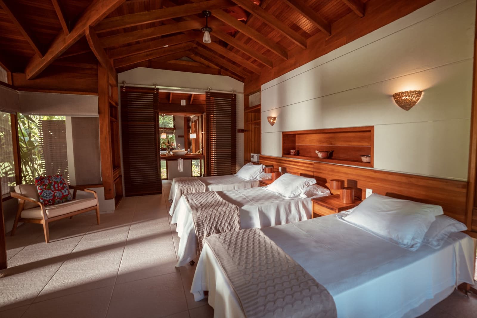Donker hout, wit linnen en het oerwoud om de hoek. Tweepersoonskamer in Cristalino Jungle Lodge met gewelfd houten plafond, warme wandlampen, houten hoofdbord en uitzicht op de tropische tuin door jaloezieedeuren