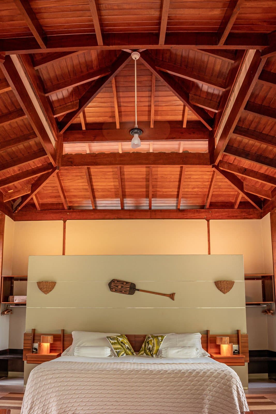 Hoge balken, warm hout en een peddel aan de muur, een kamer die weet waar ze staat. Een hoog gewelfd houten plafond overspant een tweepersoonsbed in Cristalino Jungle Lodge, geflankeerd door houten nachtkastjes met kaarslicht en een decoratieve peddel aan de hoofdbordwand